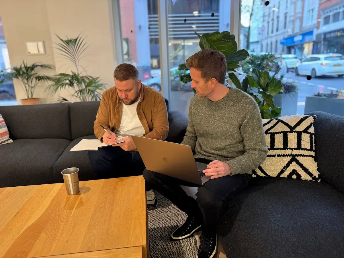 Rikki and Mark on a sofa with a laptop and notebook, scoping a build