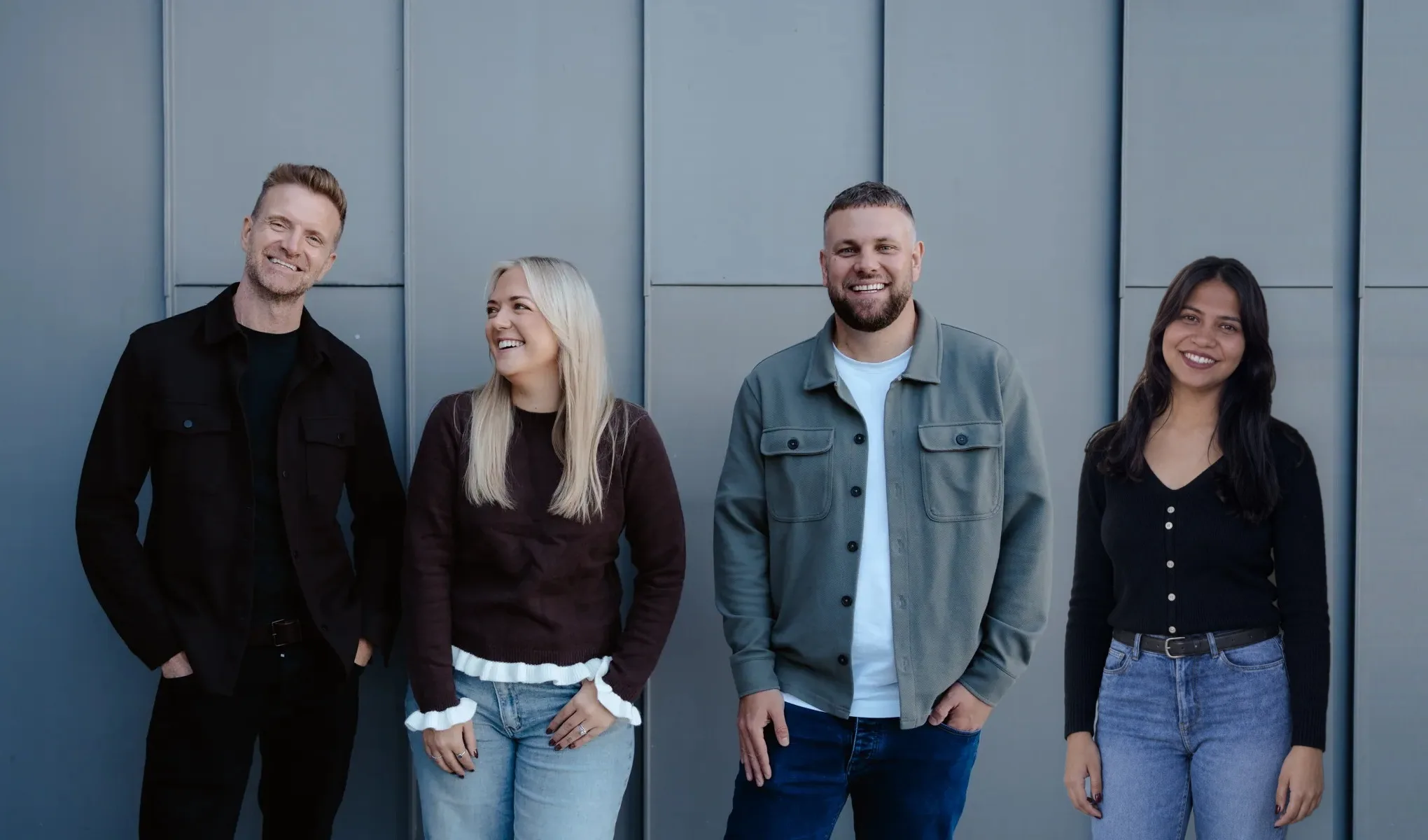 Mark, Emma, Rikki and Ishika standing against a grey wall
