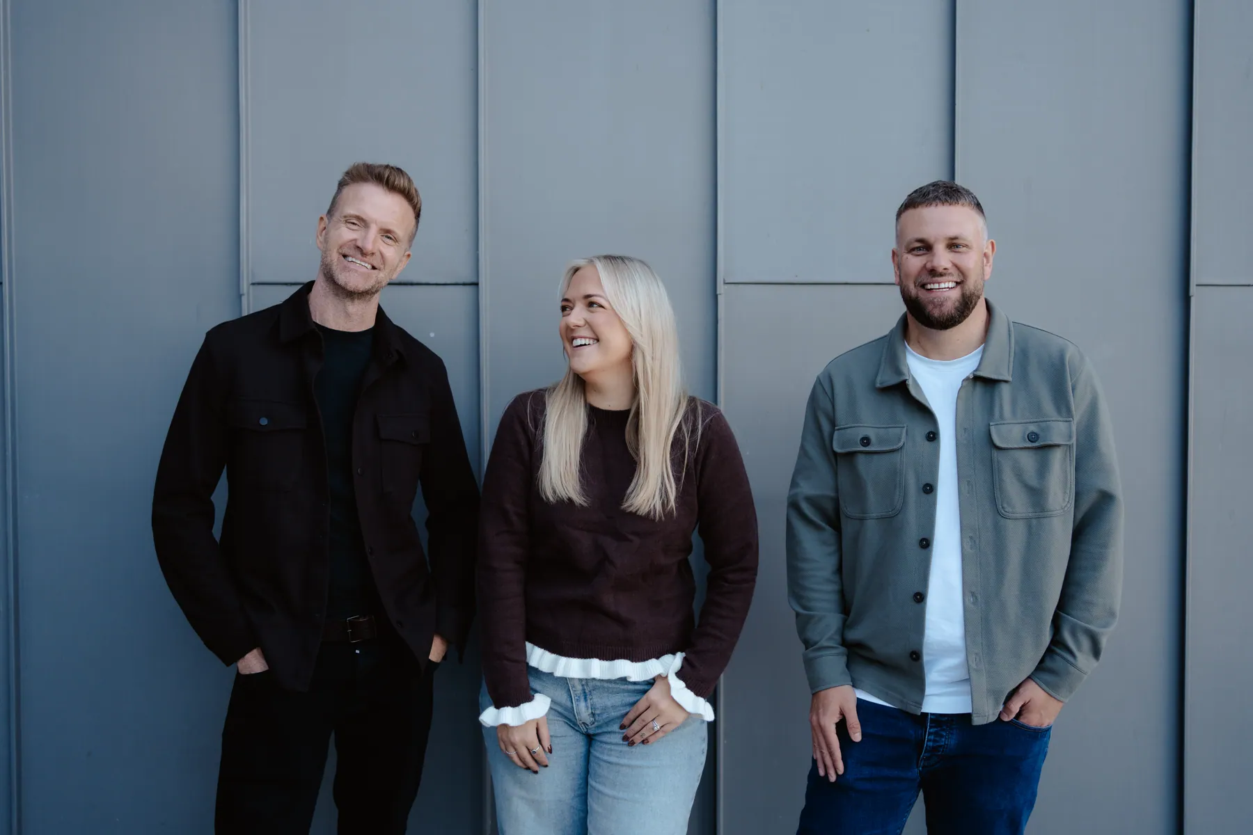 Mark, Emma and Rikki standing against a grey wall